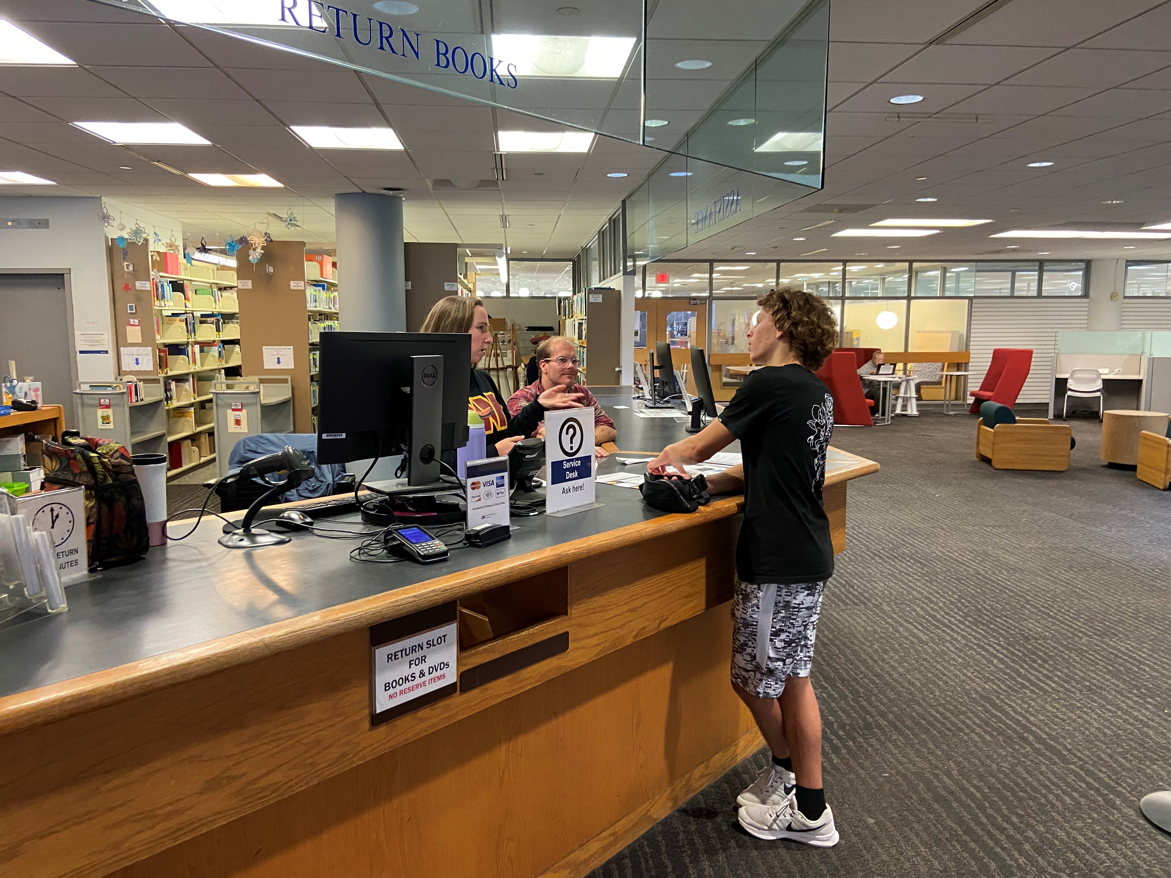 A student stands at the service desk in Hagerty Library and talks with DUL staff